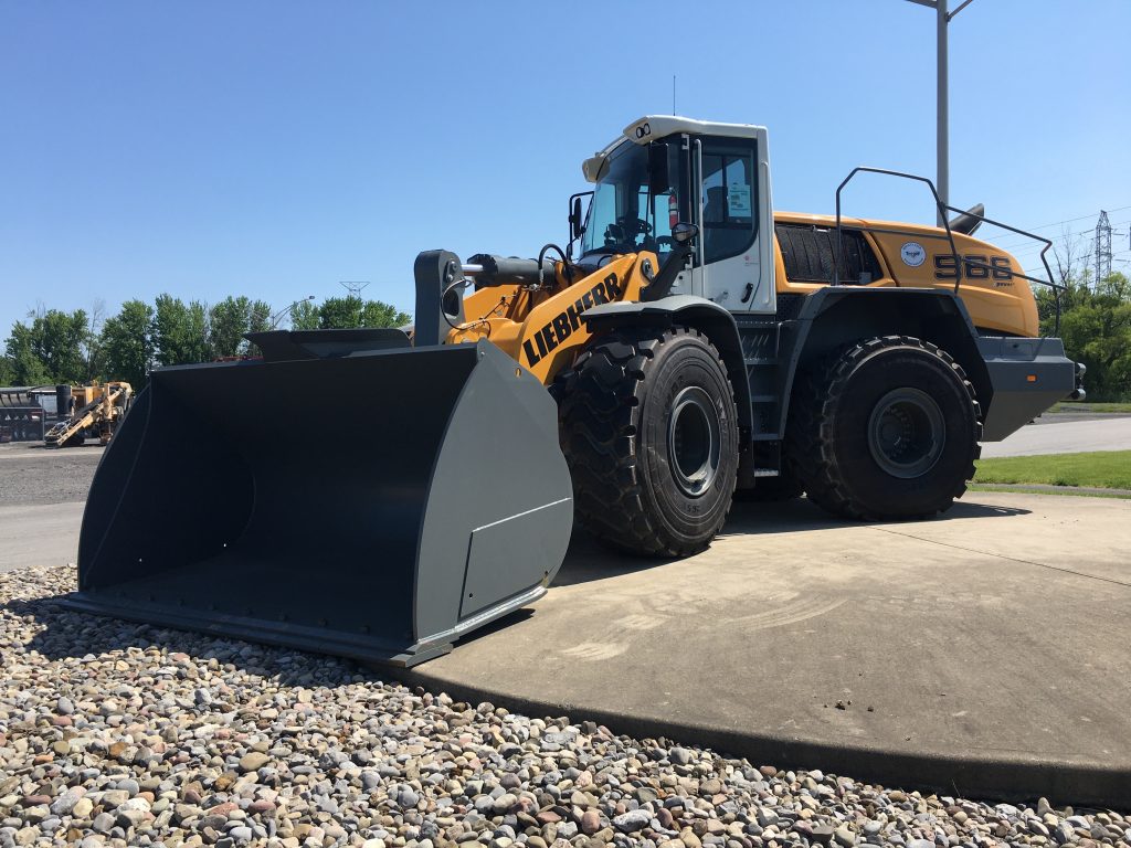 A 2019 Liebherr L566XP wheel loader with a large bucket parked on gravel, showcasing its robust tires and powerful build.